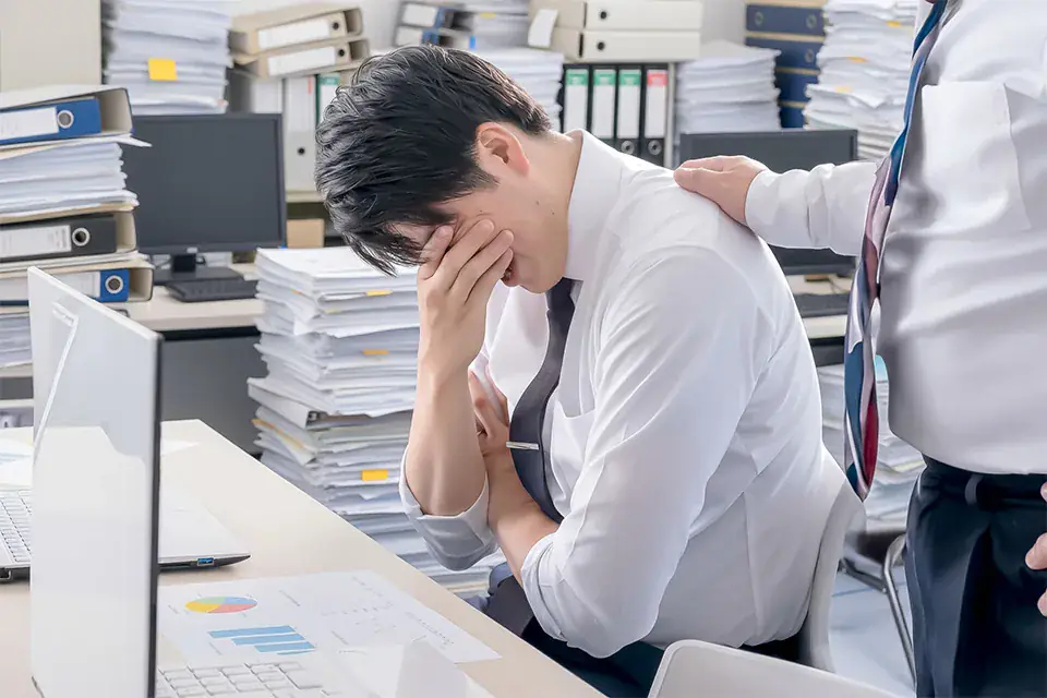 書類に埋もれて頭を抱えるフリーランスSEO担当者